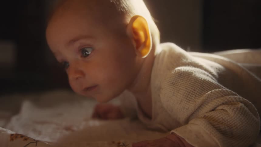 Close-up of a curious infant during tummy time, backlit by warm sunlight and looking around with wide-eyed wonder