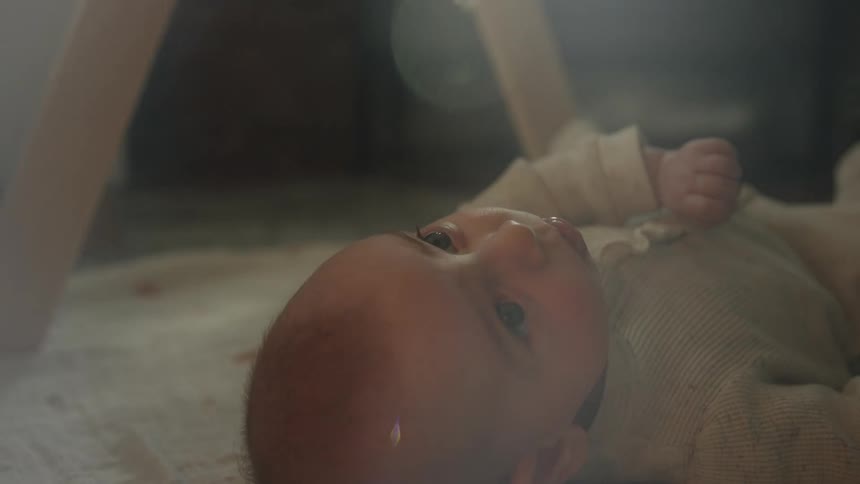 An adorable baby gazes upwards with wide eyes while lying on the floor, bathed in soft, dreamy light