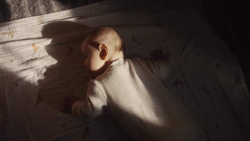 A serene overhead view of a baby in a onesie sleeping peacefully on a bed in a ray of golden sunlight