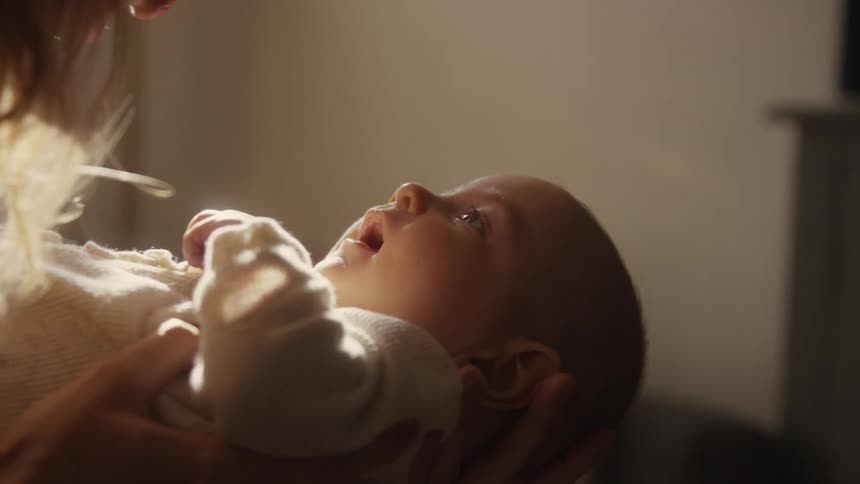 A loving mother holds her newborn baby, who looks up at her with wonder in a softly lit, warm room