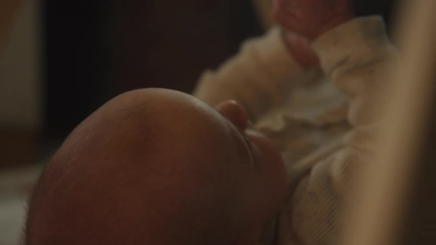 An intimate, soft-focus close-up from above shows a newborn baby resting quietly