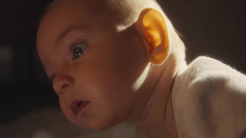 Intimate slow-motion close-up of a baby's profile as their expression changes from wonder to sleepiness in warm sunlight