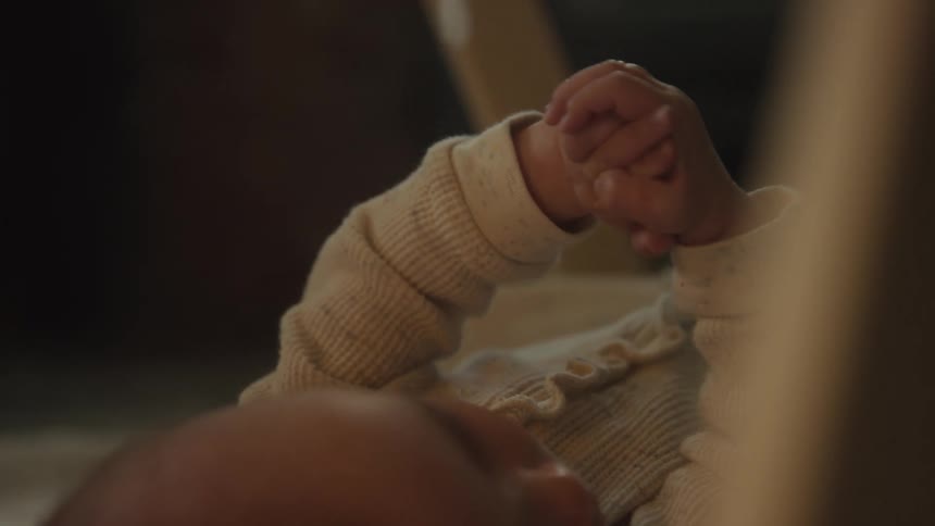 A serene close-up shot shows a newborn baby's tiny hands as they gently move and clench