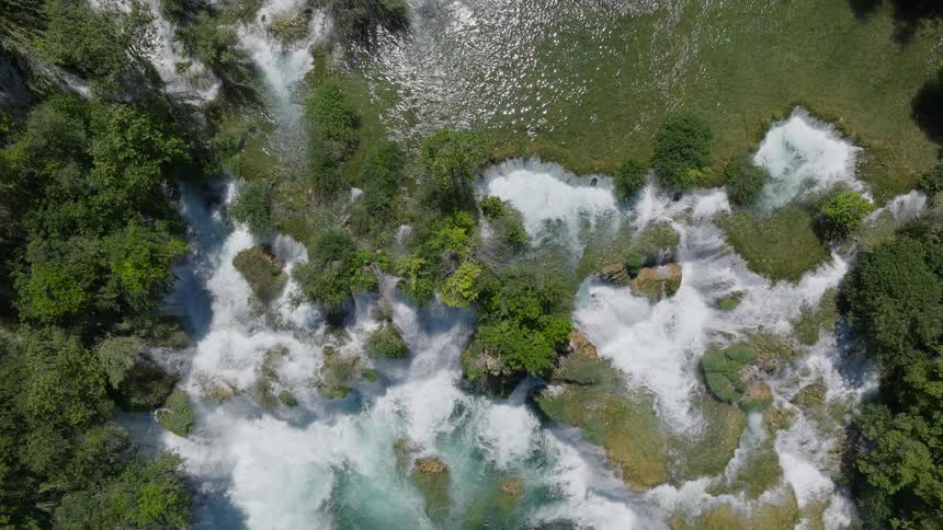 A stunning top-down aerial view captures the powerful rapids of a multi-tiered waterfall flowing through a lush green forest