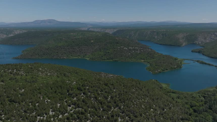 An expansive aerial shot slowly pans across a beautiful wide river winding through a lush green forest valley on a sunny day