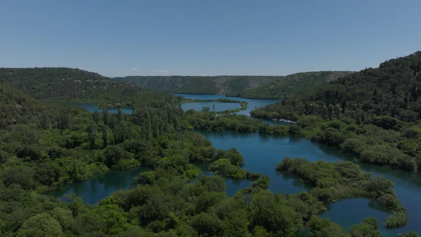 A beautiful aerial shot slowly glides forward over a stunning blue river winding through a lush, green forest valley