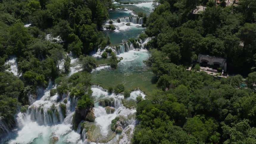 A stunning aerial reverse shot over the beautiful cascading waterfalls of Skradinski Buk in a lush green forest in Croatia