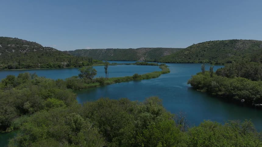 Aerial drone footage flies over a dense green forest to reveal a serene blue river winding through a valley