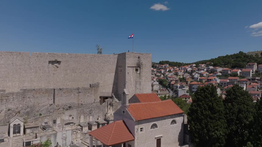 Aerial view flying over a hillside cemetery towards St. Michael's Fortress, revealing the historic city of Sibenik, Croatia