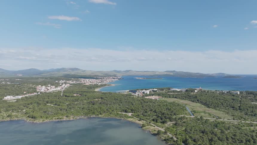 A vast aerial landscape shot of the Croatian coast, featuring a coastal town, a serene lake, and the expansive Adriatic Sea under a sunny sky
