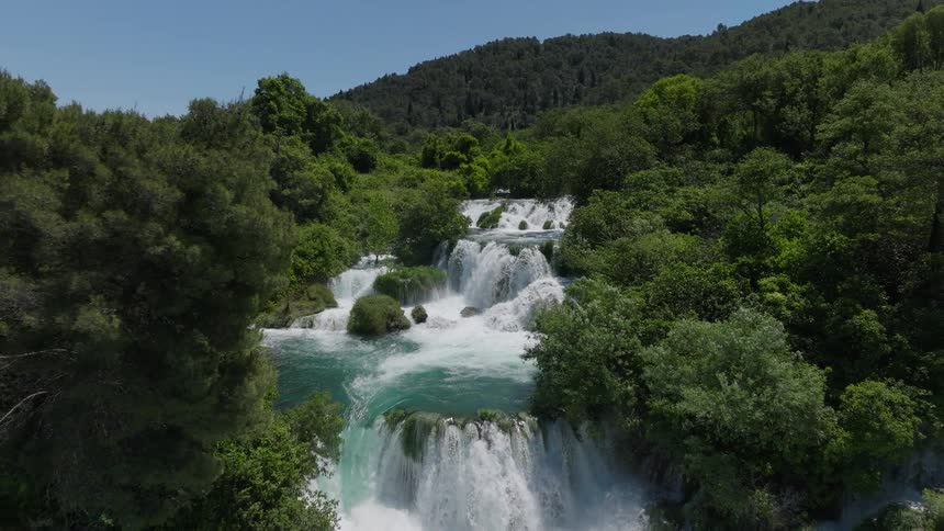 Spectacular aerial pull-back shot revealing a series of beautiful cascading waterfalls in a lush, green national park