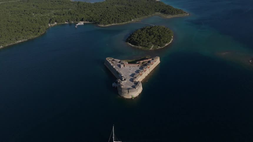 An aerial view reveals a sailboat passing the historic St. Nicholas' Fortress, a UNESCO World Heritage Site, in the stunning Adriatic Sea off the coast of Croatia