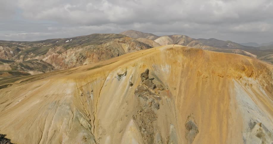 Epic aerial footage flies over the stunning, colorful volcanic mountains of the Icelandic highlands as people hike along a high ridge