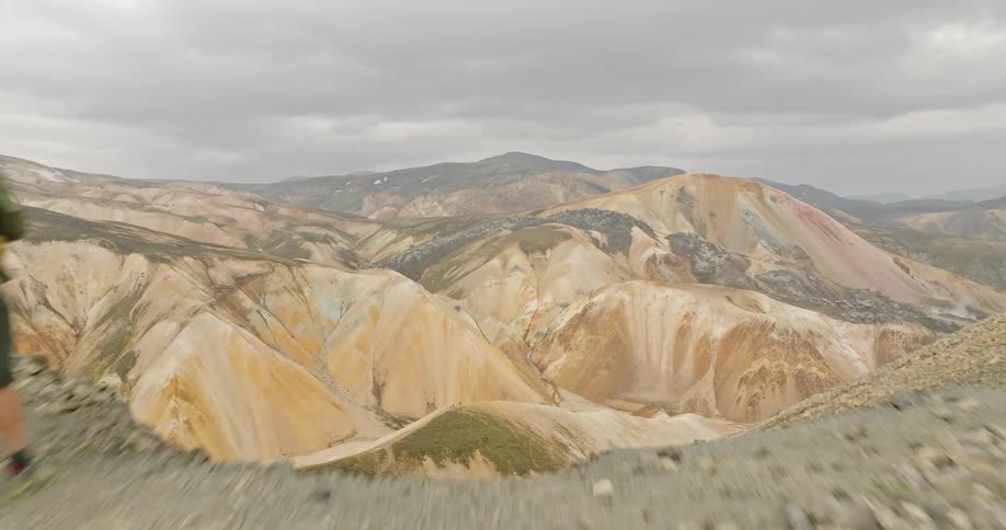 An aerial shot pushes past two hikers on a ridge to reveal a breathtaking panoramic view of the colorful Landmannalaugar mountains in Iceland