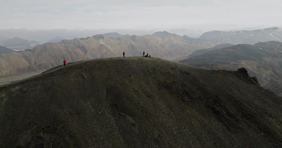 An epic aerial shot rises to reveal a vast mountain range behind a group of hikers on a desolate peak in Iceland