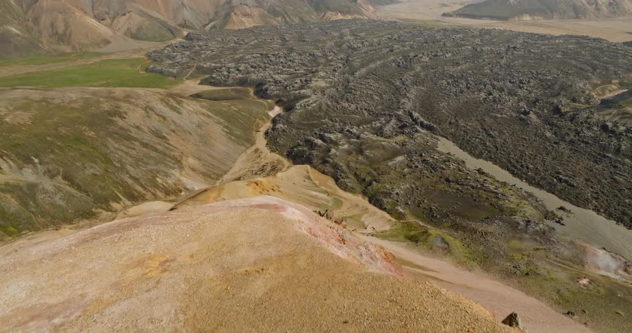 A drone follows two hikers walking on a barren mountain ridge, tilting up to reveal a stunning volcanic landscape in Iceland