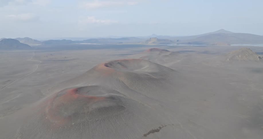 A static aerial shot captures the otherworldly landscape of dormant volcanic craters in a desolate, ash-covered valley