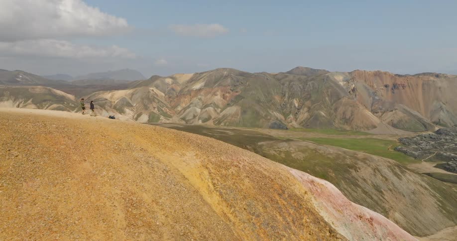 Two hikers walk along a golden mountain ridge revealing the stunning multicolored rhyolite mountains of Landmannalaugar in Iceland