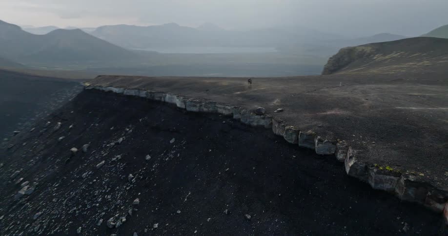 Epic aerial footage follows a hiker along the rim of a vast volcanic crater, revealing a stunning deep blue lake inside