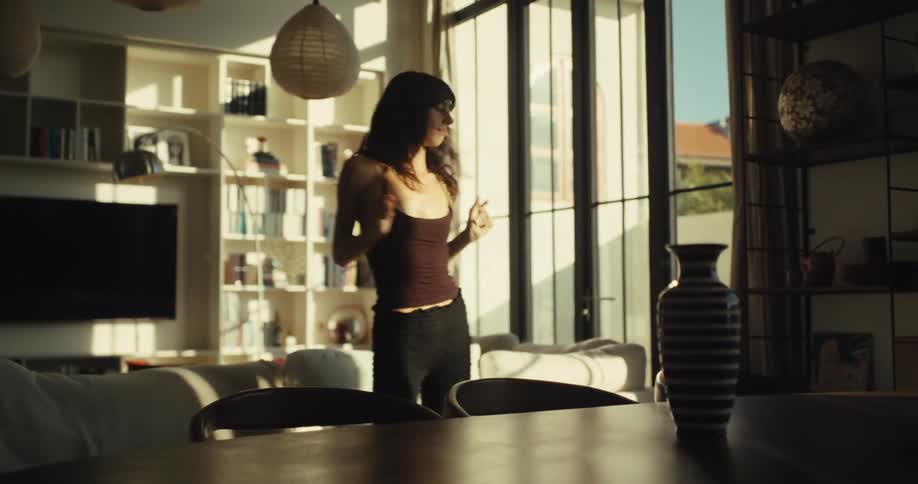 A carefree young woman dances with joy and abandon in her stylish, sun-drenched living room