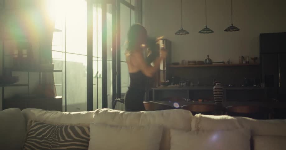 A free-spirited woman dances expressively on a dining table in her modern, sun-drenched home