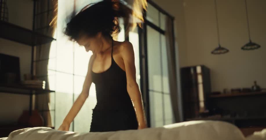Backlit by the bright morning sun, a carefree woman dances energetically in her stylish bedroom