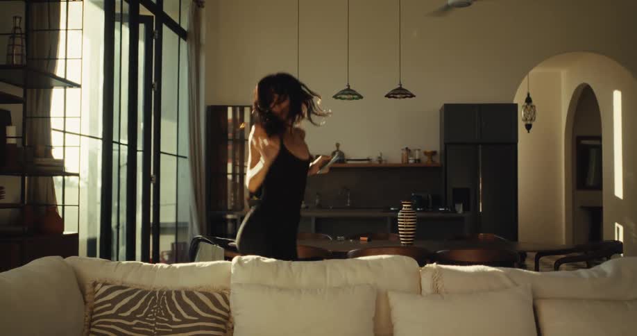 Slow motion shot of an energetic woman dancing freely to music from her smartphone in a stylish, sunny home
