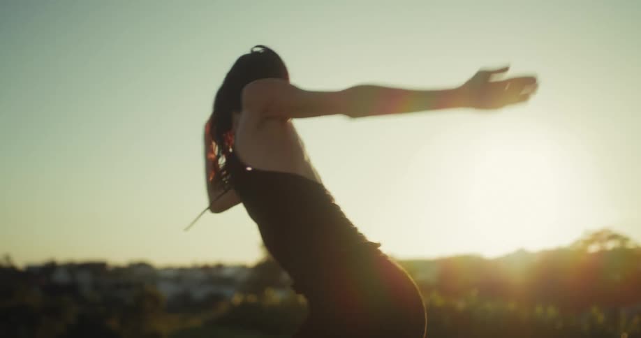 A silhouetted woman dances barefoot on a rooftop in slow motion, with the camera tilting down to her feet against the golden hour sun