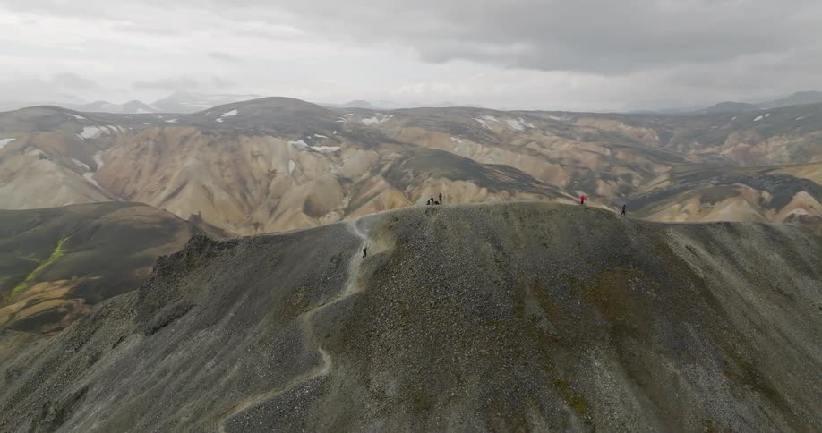 An epic aerial shot orbits a group of hikers as they walk along a narrow ridge in the breathtaking and colorful volcanic mountains of Landmannalaugar, Iceland