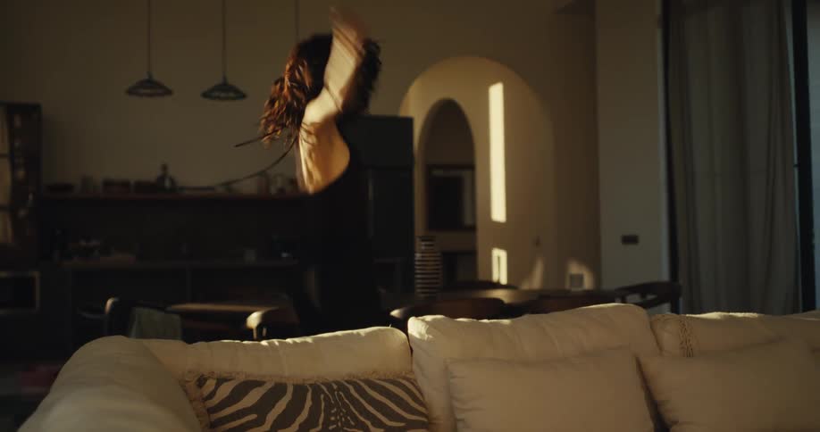 A joyous woman dances with carefree abandon in her sun-drenched living room in slow motion