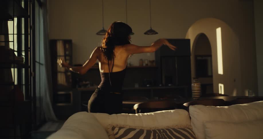 A graceful dark-haired woman dances expressively in slow motion in her beautiful, sun-drenched living room