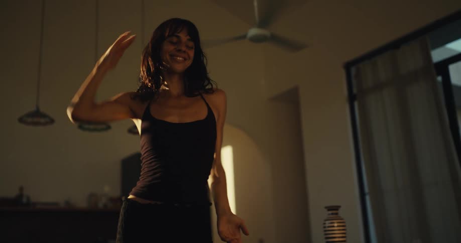 A carefree young woman dances happily and expressively in her sunlit living room, captured in slow motion