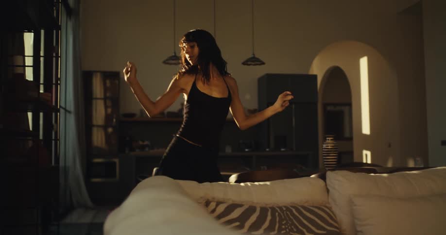 A happy woman dances freely in slow motion in the golden sunlight of her spacious modern living room