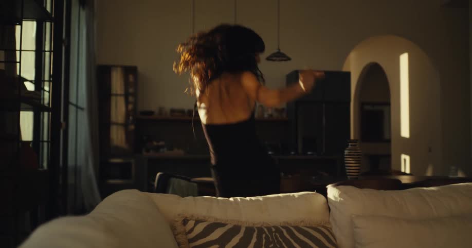 A happy brunette woman dances energetically in her stylish, sunlit living room in slow motion