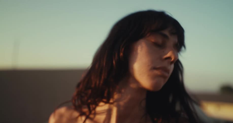 Slow motion close-up of a peaceful woman with her eyes closed, enjoying music on her earbuds as the golden sun sets