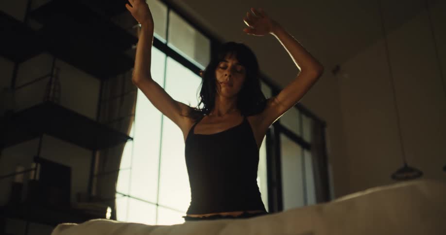 A graceful young woman dances freely and expressively in her modern loft apartment, her body silhouetted by the warm sunlight
