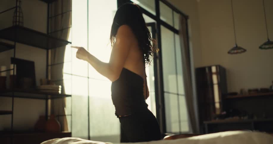 An energetic woman dances with joyful abandon in her sun-drenched living room, backlit by the bright sun