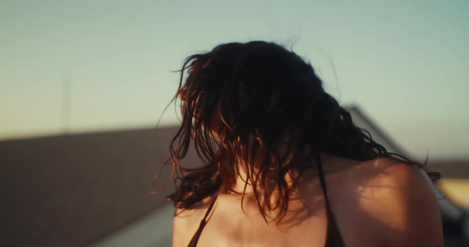A beautiful woman with wet hair listens to music on her earbuds and moves freely in the golden hour light