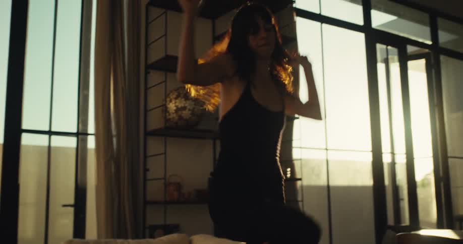 A woman joyfully dances on a couch in her sun-drenched living room in slow motion