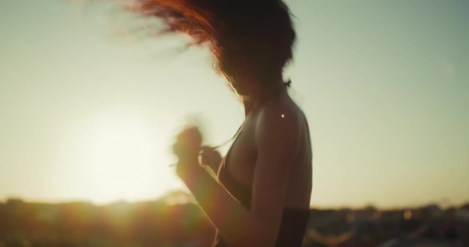 A barefoot woman dances expressively on a rooftop, silhouetted against the golden morning sun