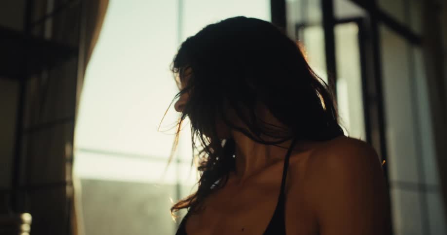 Slow motion close-up of a serene woman gracefully stretching and dancing in her apartment, backlit by a warm, golden sunrise