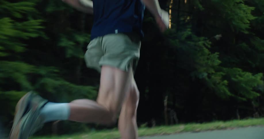 Close-up tracking shot of a fit man running on a paved road through a dark forest