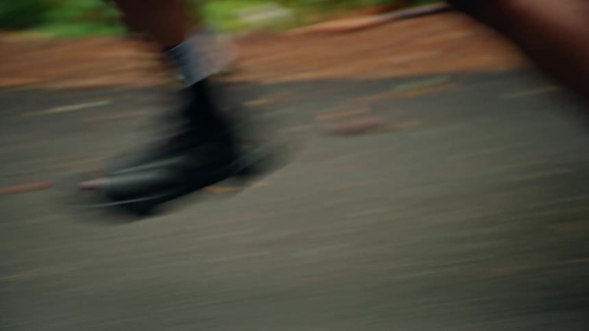 A tracking shot captures a close-up of a woman's legs and feet as she runs at a fast pace through a verdant forest
