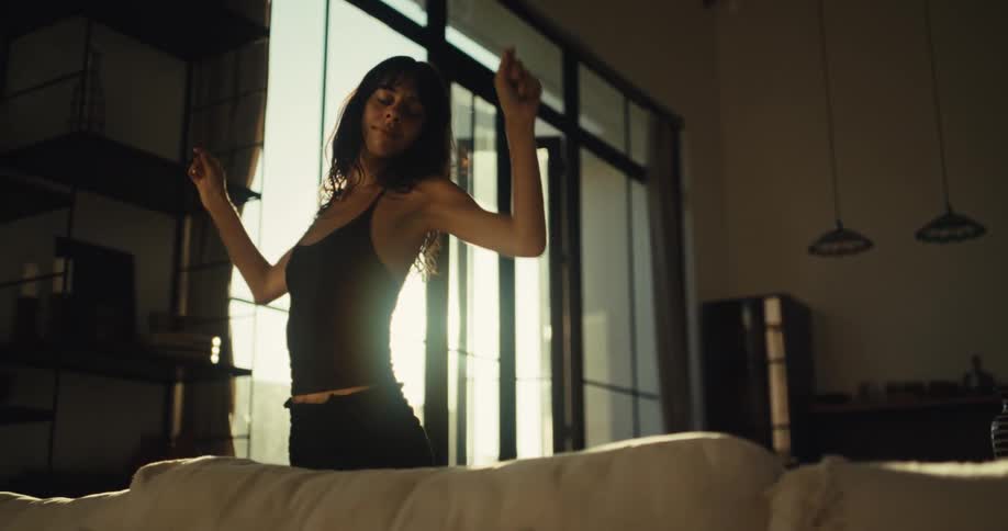 A silhouetted woman dances expressively and freely in her sun-drenched living room in slow motion