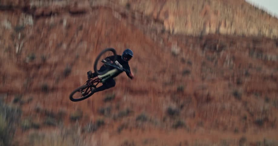 An extreme mountain biker performs a whip off a hip jump in a rugged desert landscape