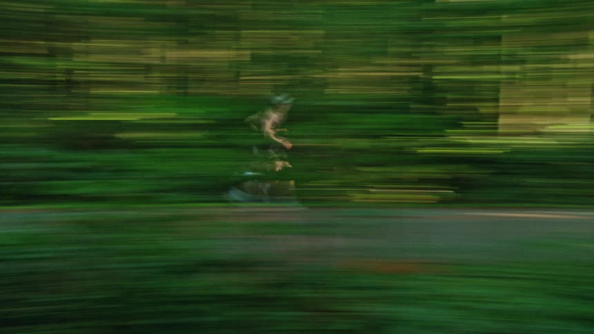 A stylized motion blur shot captures a man running on a path through a lush green forest