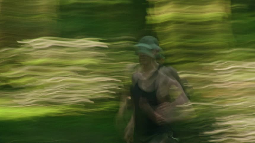 An artistic, motion-blurred view of a person trail running through a vibrant green forest