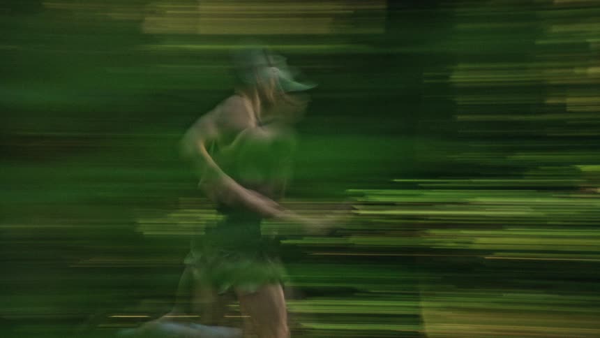 A man running through a lush green forest is captured in an artistic, impressionistic style with a slow shutter speed creating motion blur
