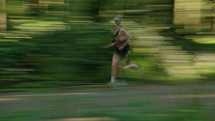 A male athlete runs on a path through a lush forest in a stylized shot with a strong motion blur effect