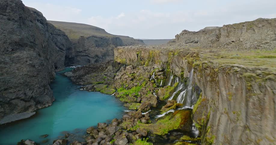 An epic aerial flight through a rugged Icelandic canyon reveals stunning waterfalls cascading into a vibrant turquoise river